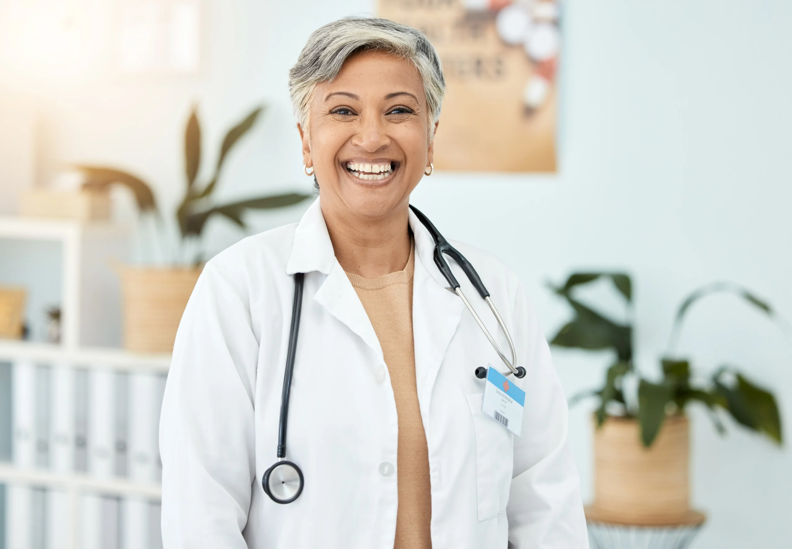 Female POC doctor in a clinic wearing a lab coat with stethoscope smiling at the camera.