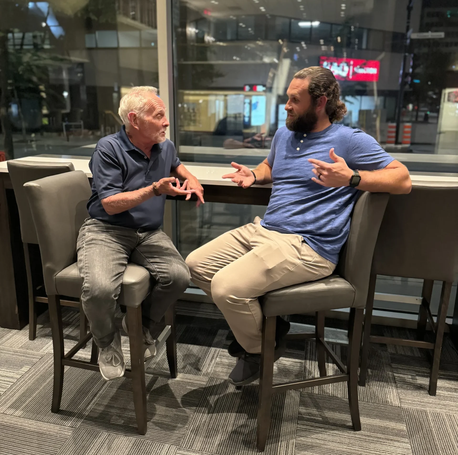 Medicare experts, Arnie and Jesse, a father and son team, chat seated in their insurance office building.