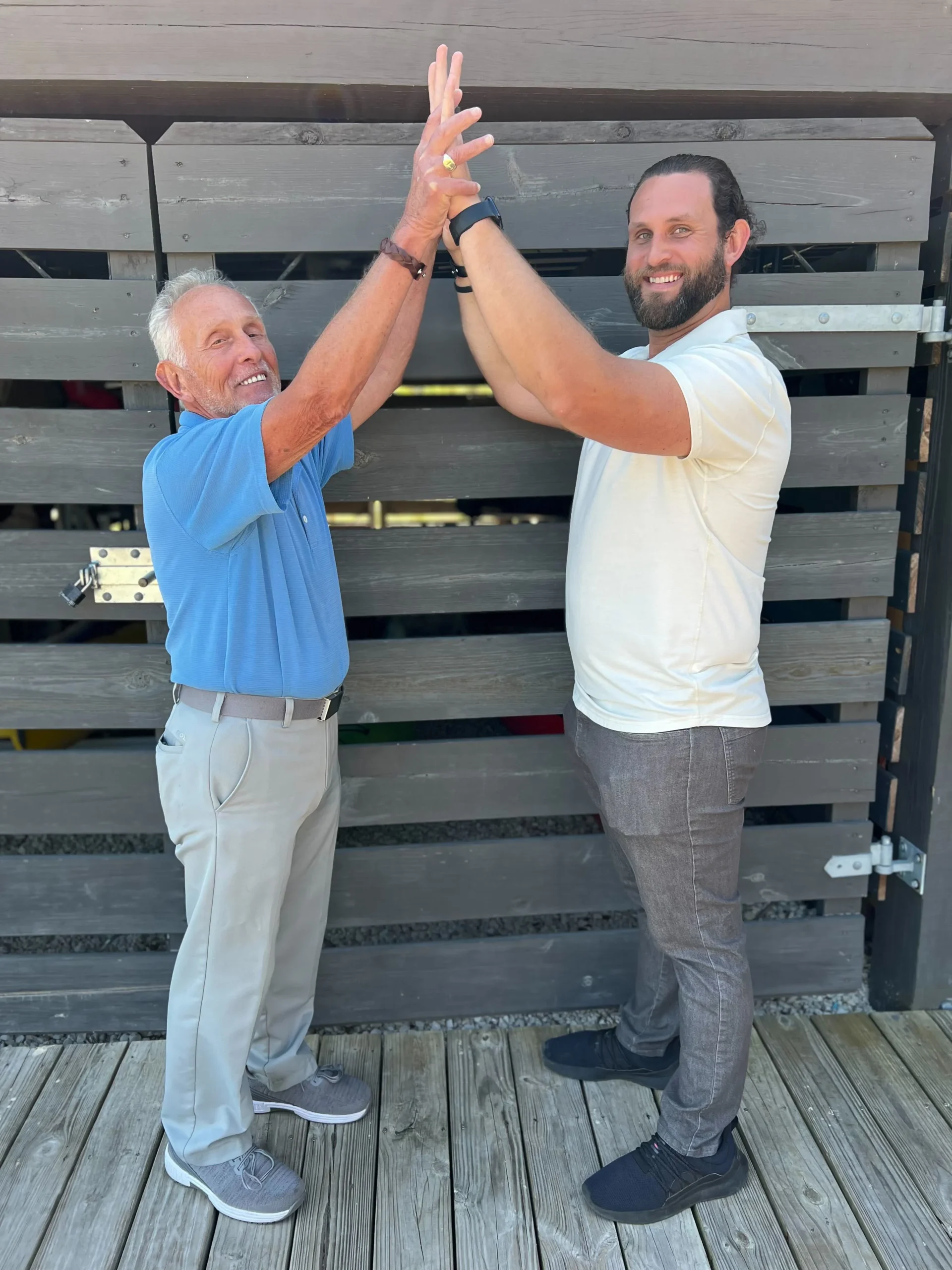 Arnie and Jesse, a father and son insurance brokerage, high-fiving outdoors.