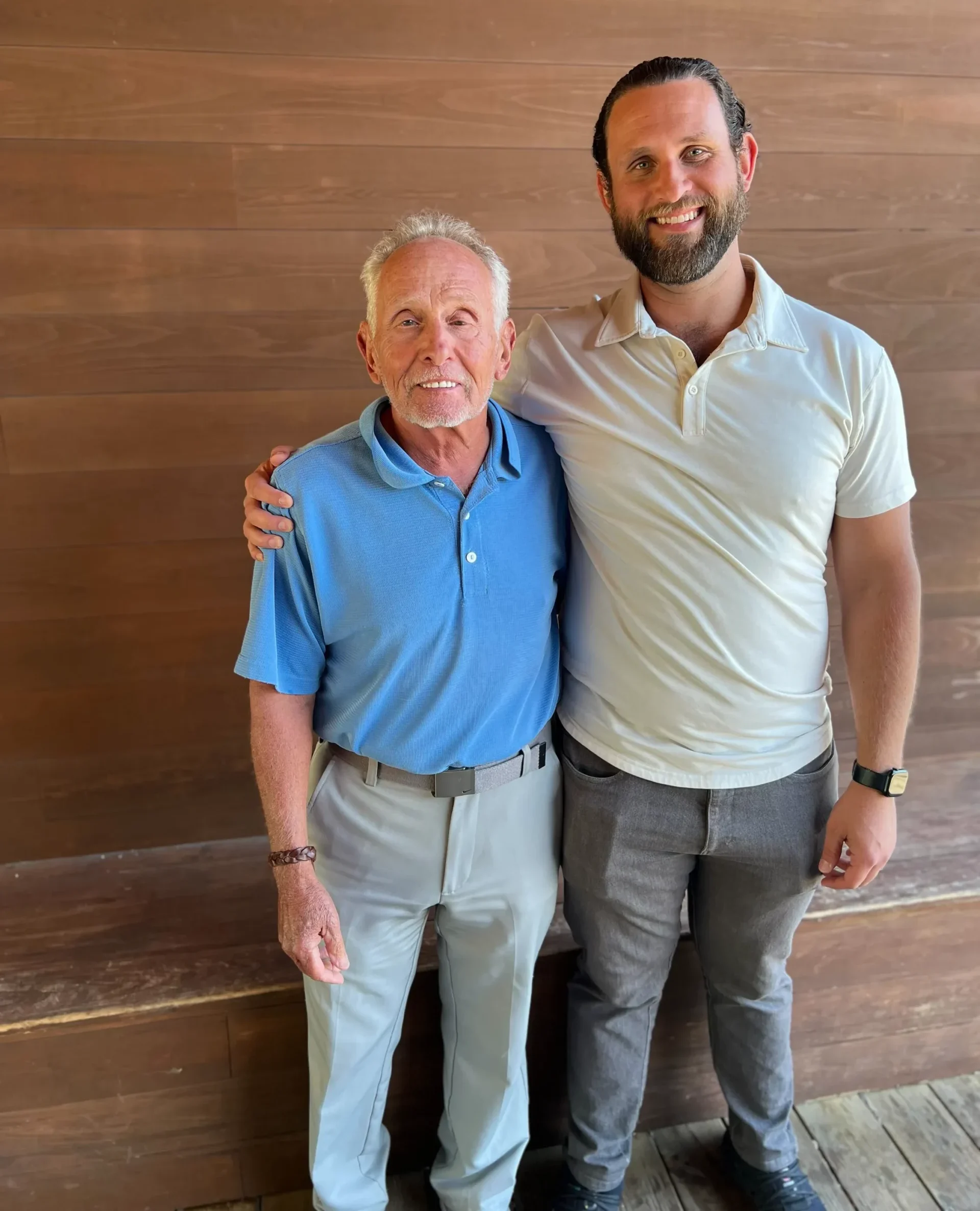 Arnie and Jesse, a father-and-son Medicare team, hugging with a wooden background.